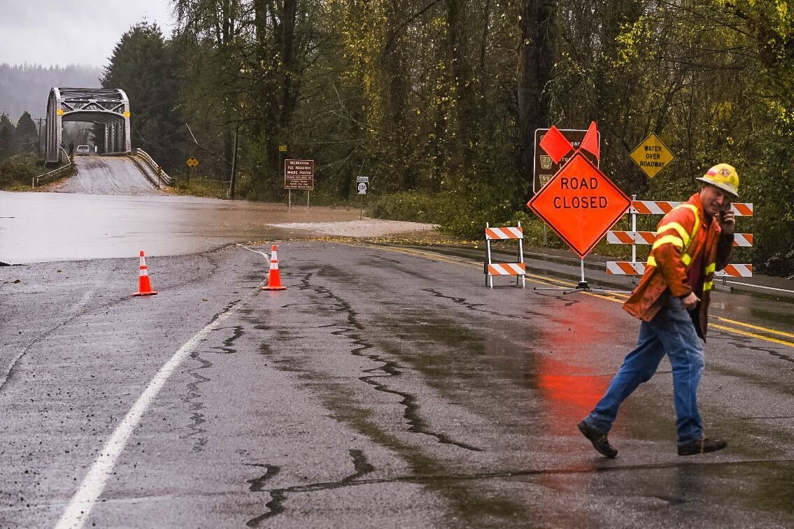 A member of the Washington State Department of Transportation talks on the phone while crossing Cispus Road as the Cowlitz River flows over closing the roadway.